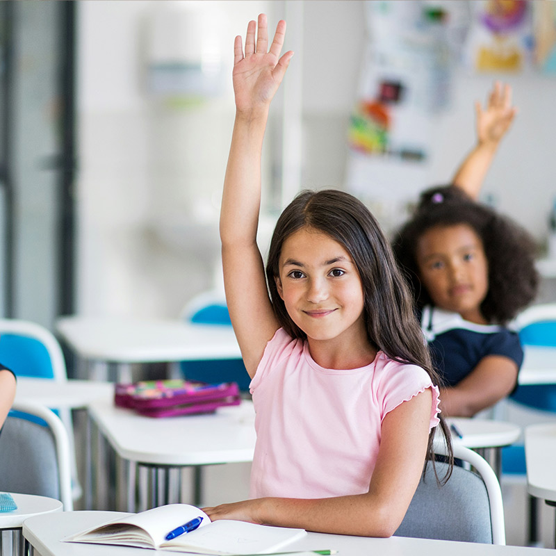 young-children-in-classroom-raising-their-hands-smiling